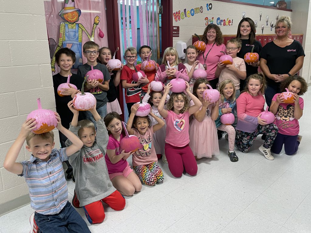 Group of students holding pink pumpkins next to teachers in hallway