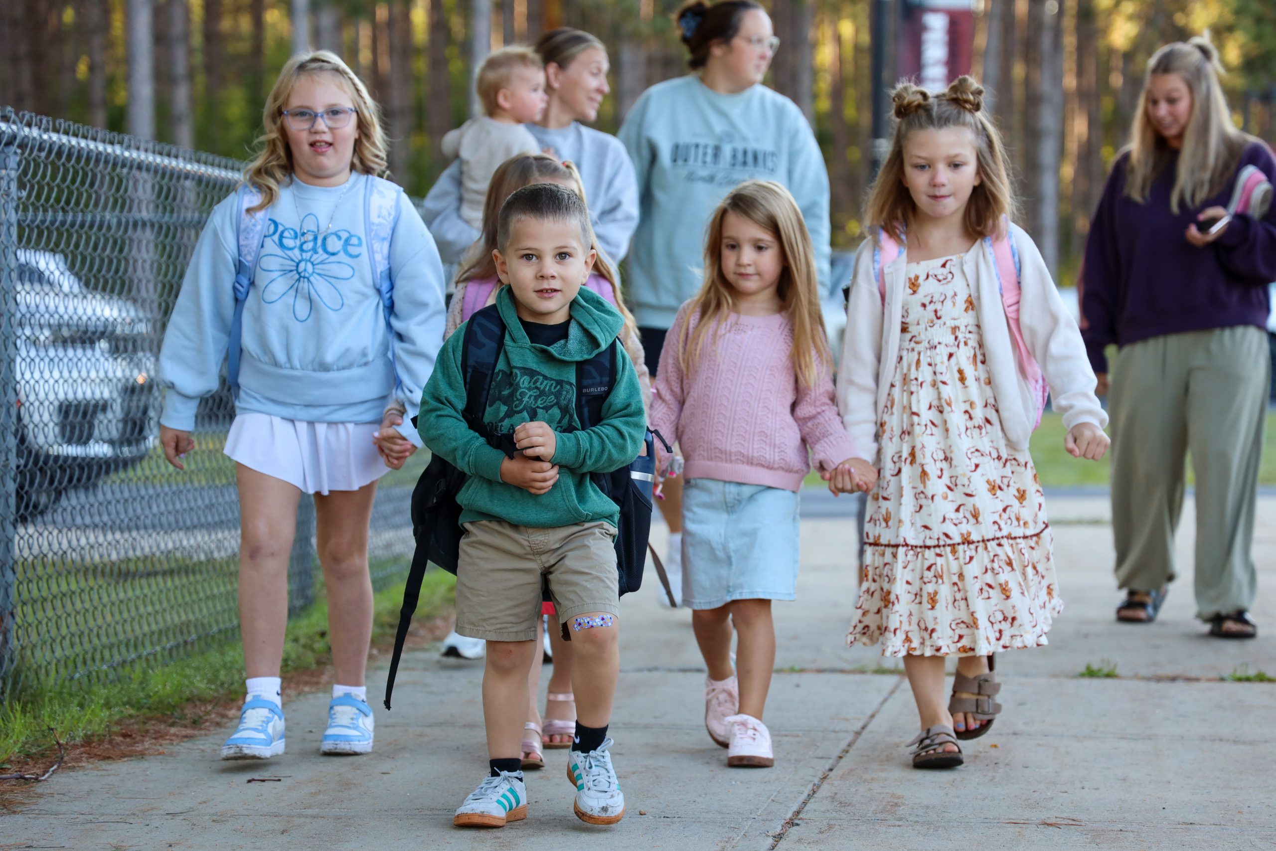 Several students walking on a sidewalk with adults