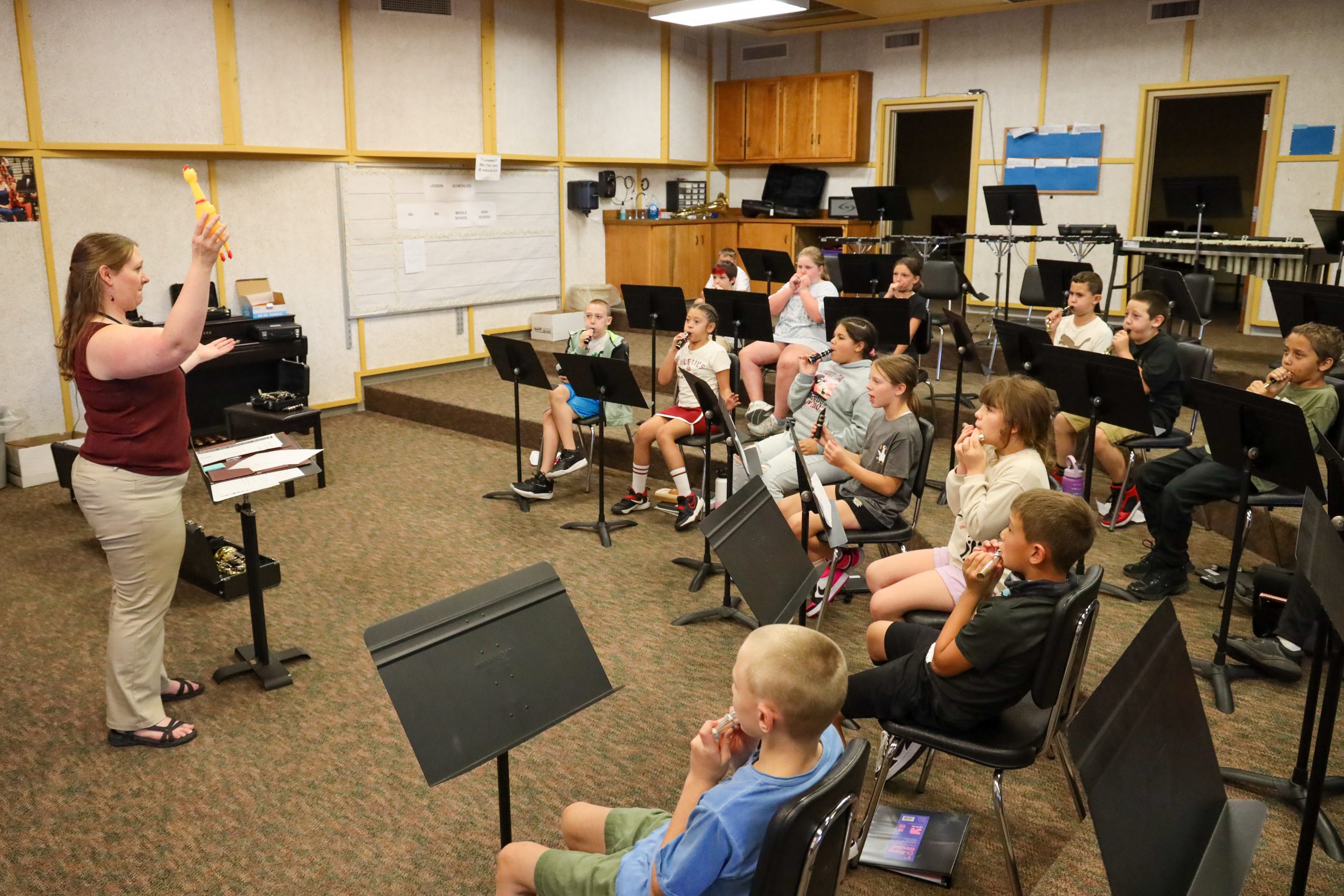 A teacher holding a rubber chicken standing in front of students in a music room