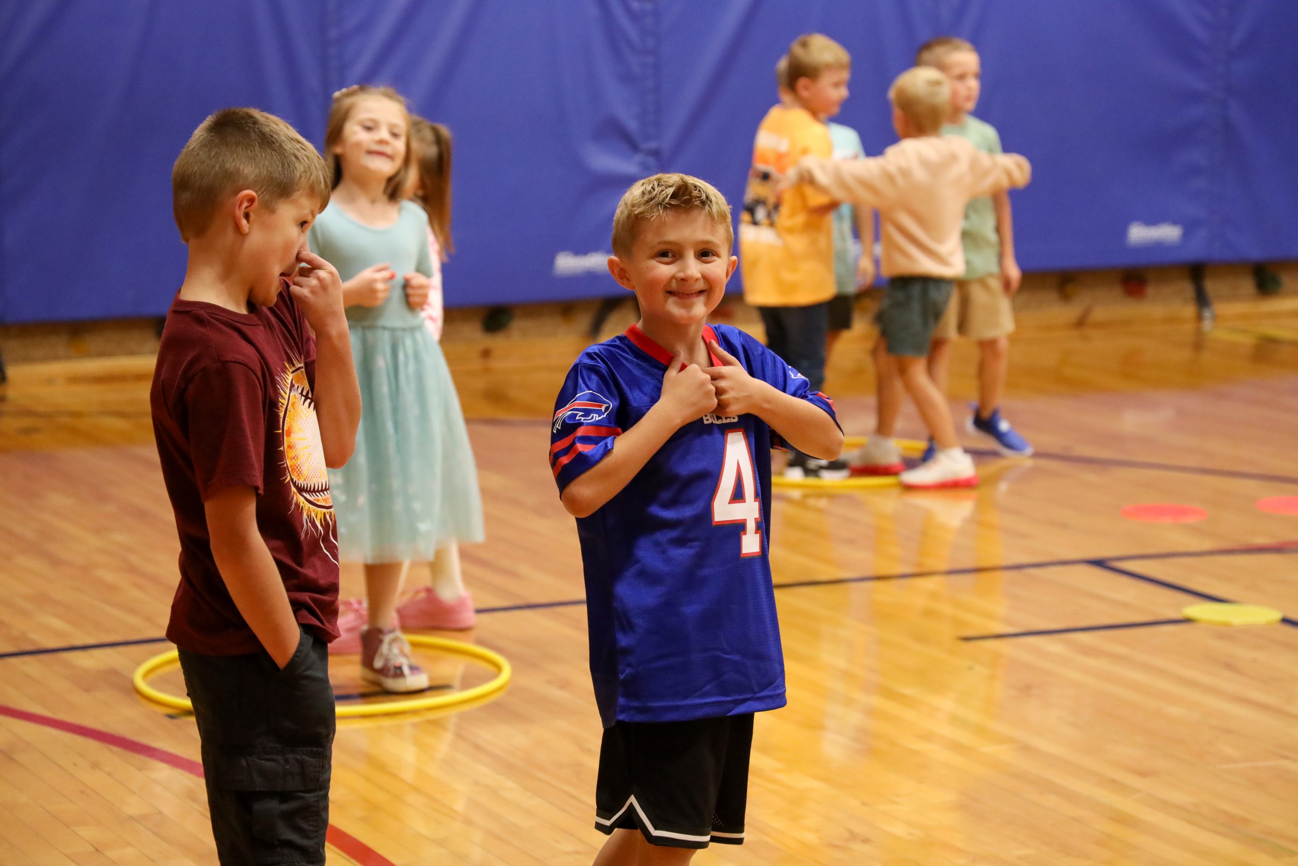 A boy holding thumbs up in a gym of students