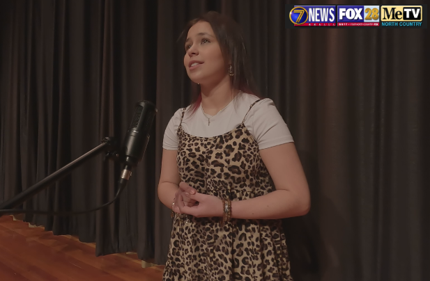A teacher holding a rubber chicken standing in front of students in a music room