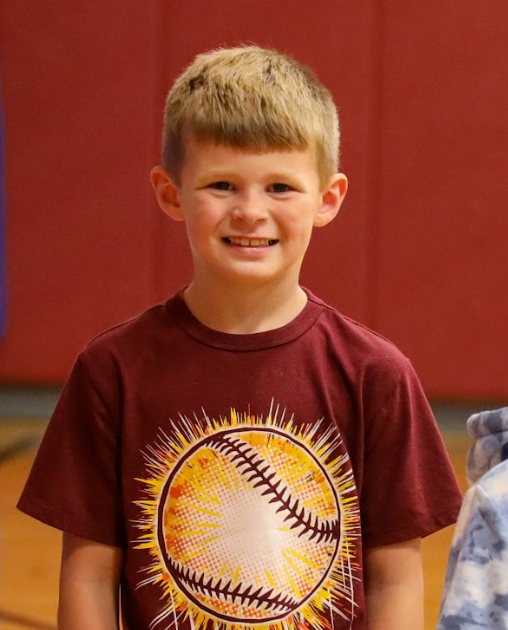 A boy holding thumbs up in a gym of students