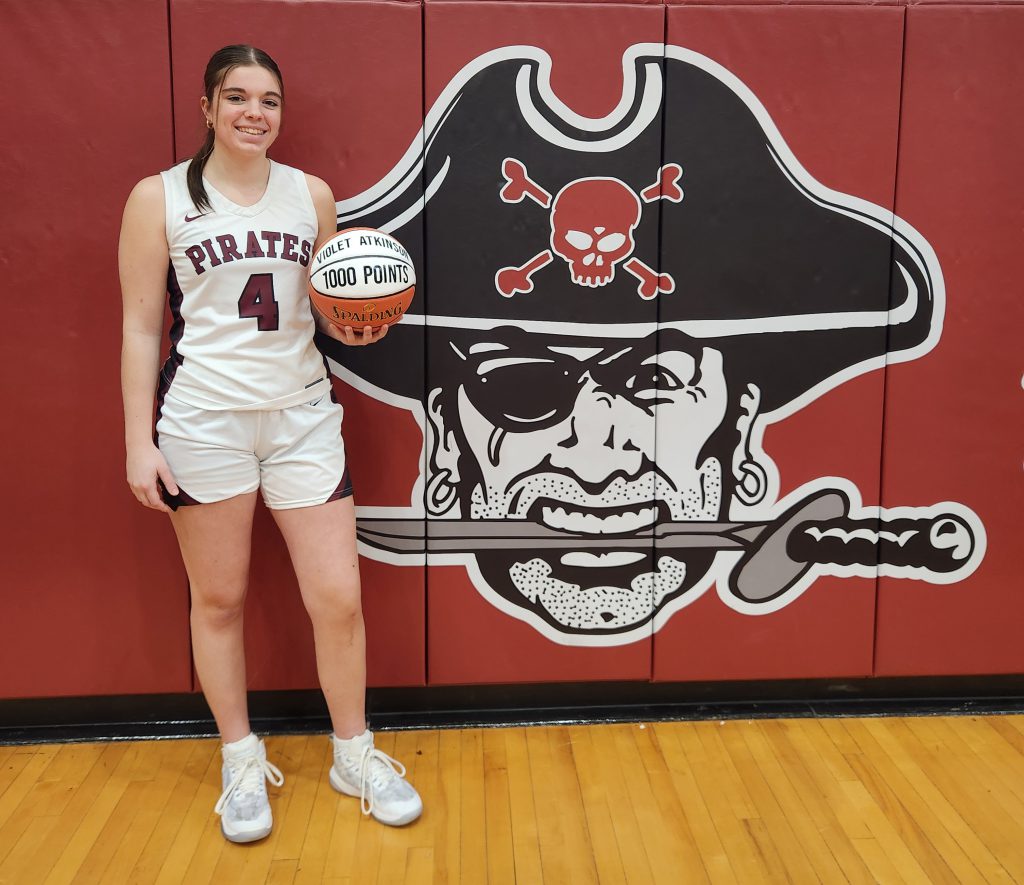 A student holds a basketball while standing in the gym in front of the HCS pirate logo.