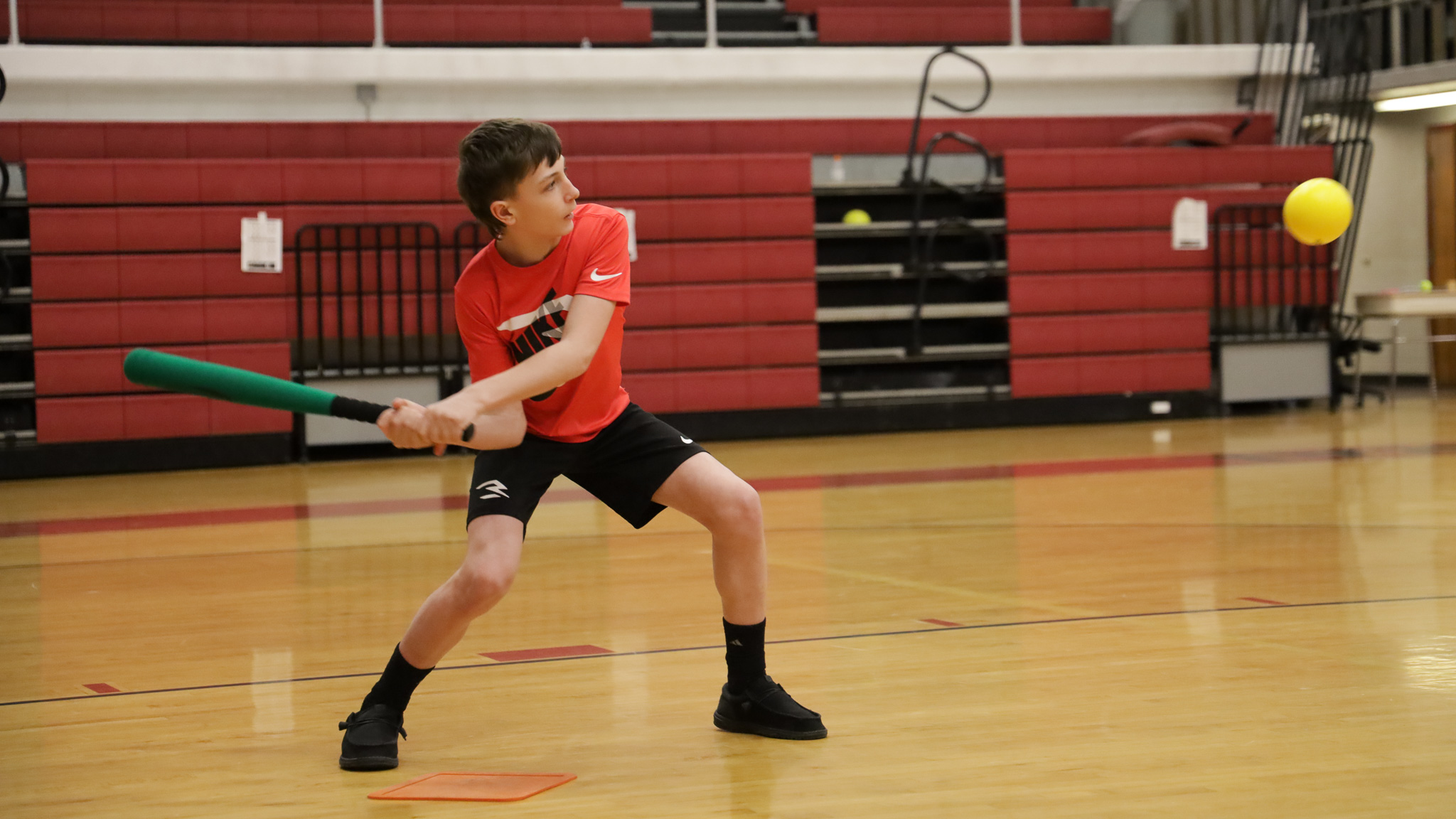 A student swings a baseball bat in the gym.