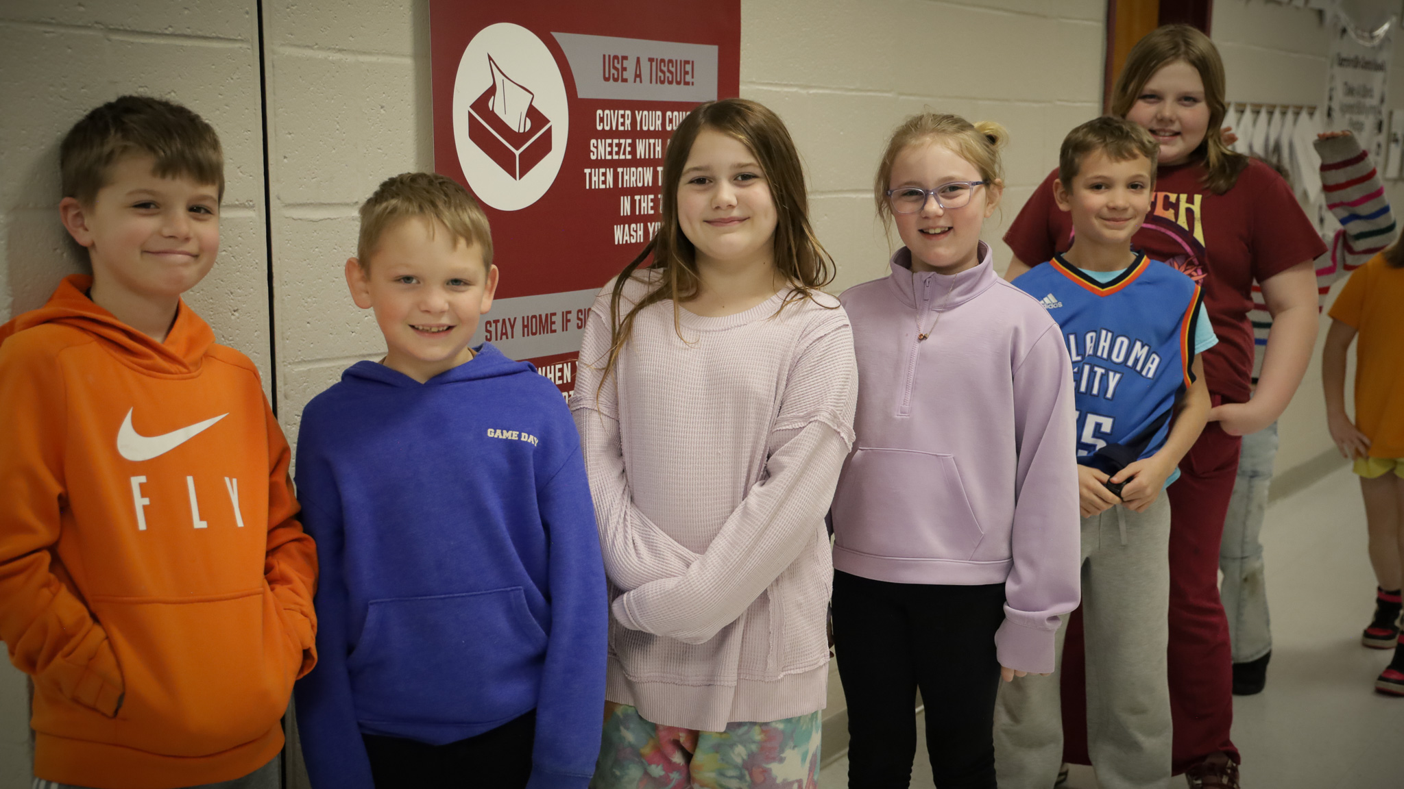 Students stand in a line and smile in a hallway.