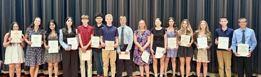 National Honor Society inductees stand in a line holding their certificates.